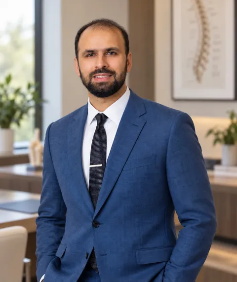 Dr. Padela in a blue suit, standing in an office with a spine illustration on the wall